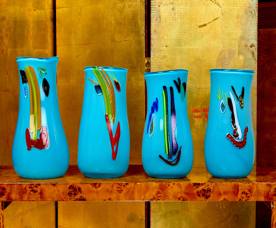 Four blue vases with colorful abstract designs on a wooden surface.