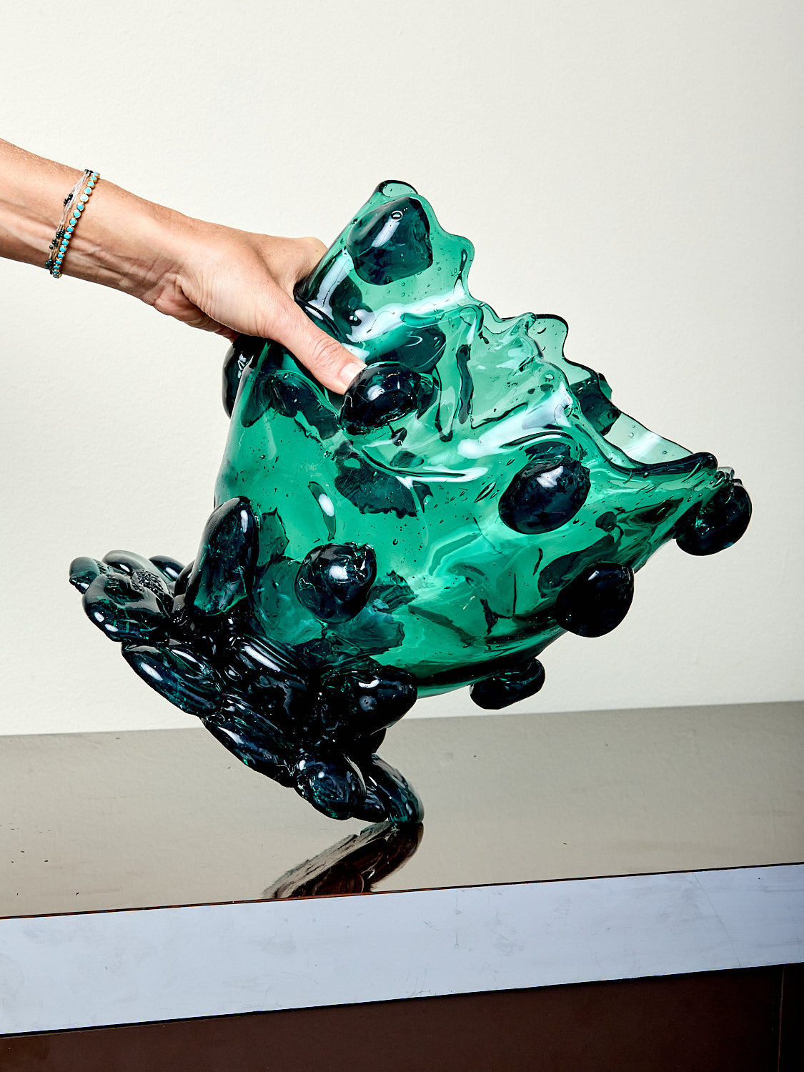 Hand holding a green resin sculpture on a reflective surface with a neutral background
