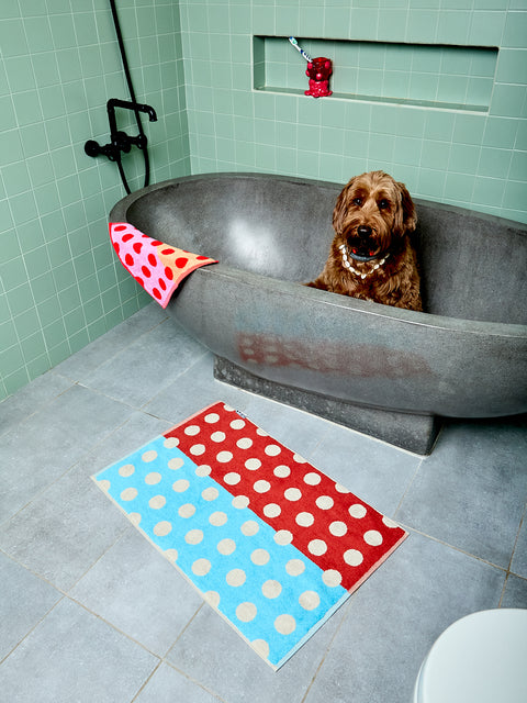 Dog in a bathtub with polka dot towels on a tiled bathroom floor.