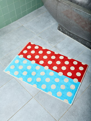 Brown and blue polka dotted bath mat on tiled bathroom floor.