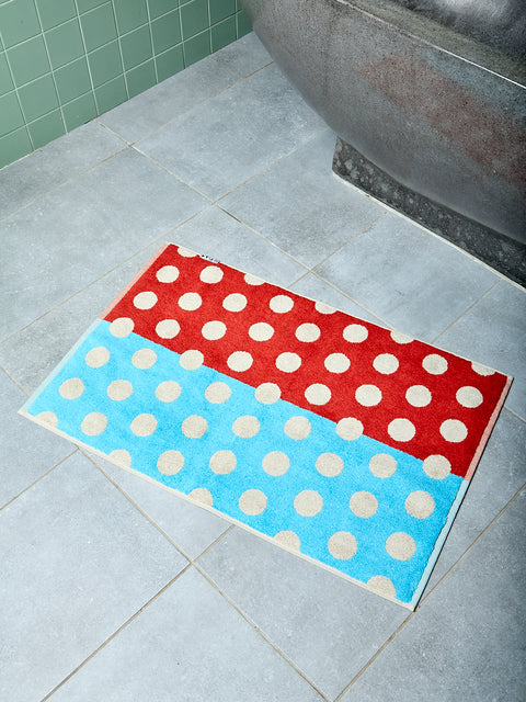 Brown and blue polka dotted bath mat on tiled bathroom floor.