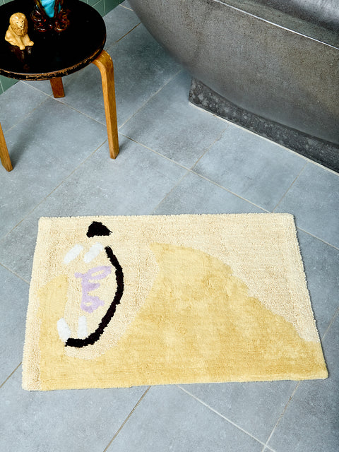 Bathmat with abstract yellow, black, white, and lavender 'Leo' design on a tiled floor