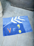 Blue doormat with white, orange, and yellow abstract designs that spell out "Virgo" on a tiled floor.