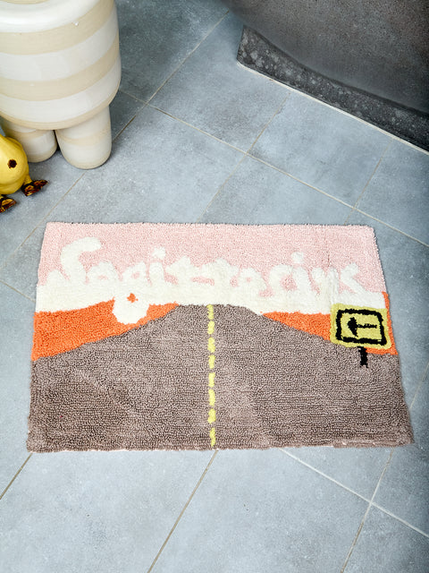 Bathmat with an open road design and text reading "Sagittarius" on a tile floor
