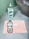 Pink bath mat with water bottle design and text reading "AQUARIUS" on a bathroom floor.