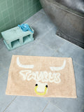 Beige bathmat with 'Taurus' design featuring bull nostrils and a pair of horns on a tiled floor