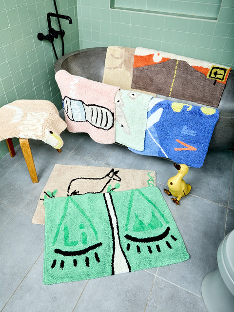 Assorted zodiac-themed bathmats on a bathroom floor and splayed over a bathtub