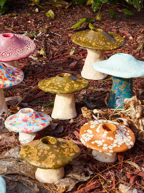 Colorful ceramic mushrooms on a garden path with leaves and plants.