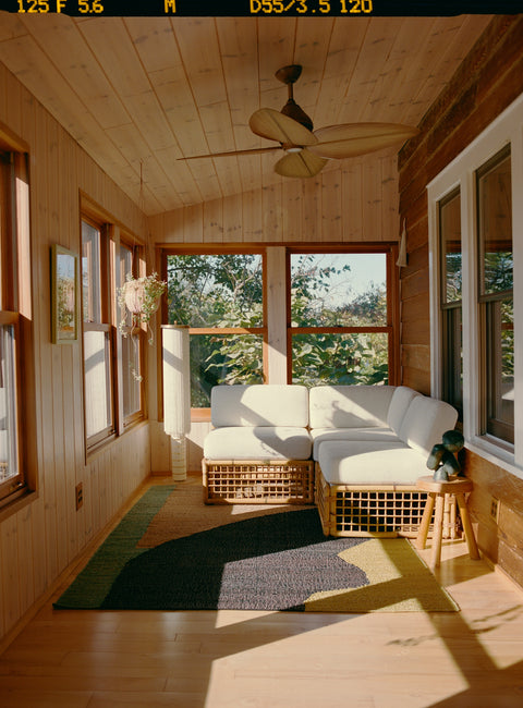 In the Arbor Rug by Cold Picnic in a sunroom with a white rattan couch.