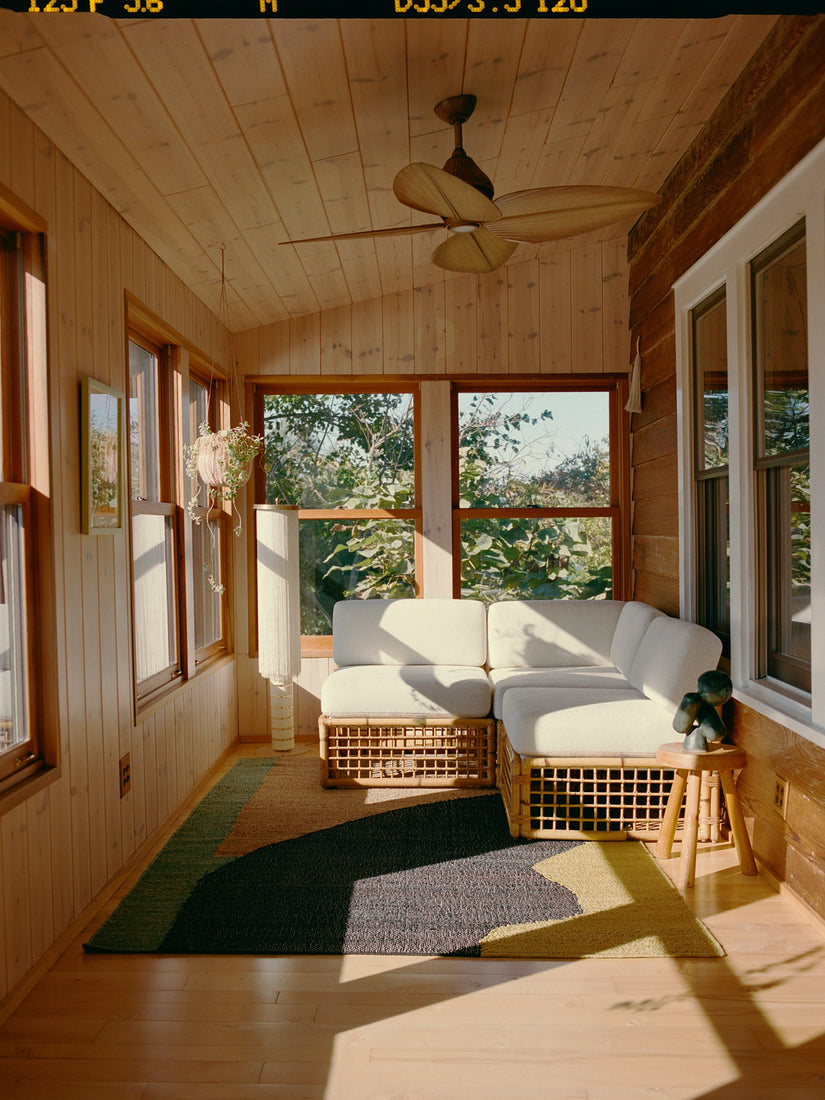 In the Arbor Rug by Cold Picnic in a sunroom with a white rattan couch.