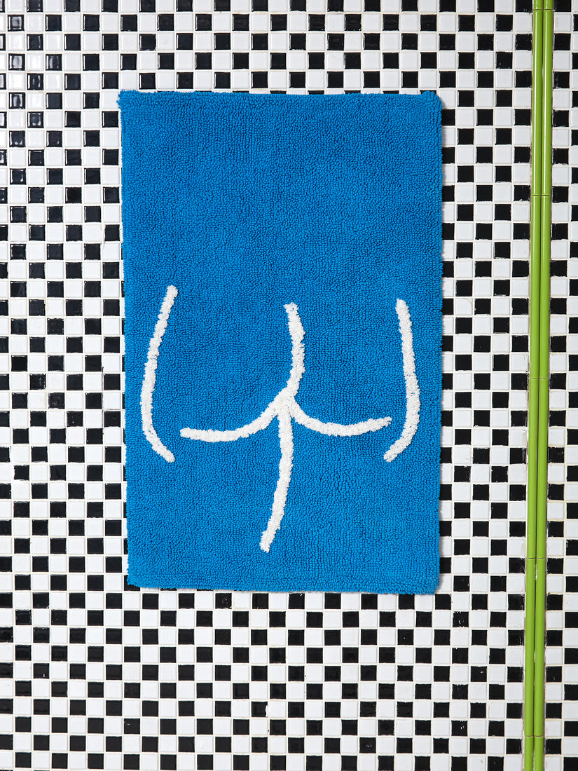 A blue tushy bathmat against black and white checkered tile.
