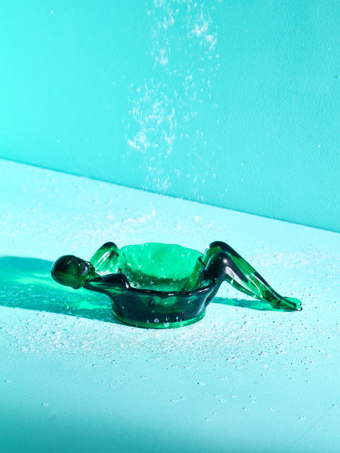 An emerald green bathing lady dish with white glitter being poured over it.