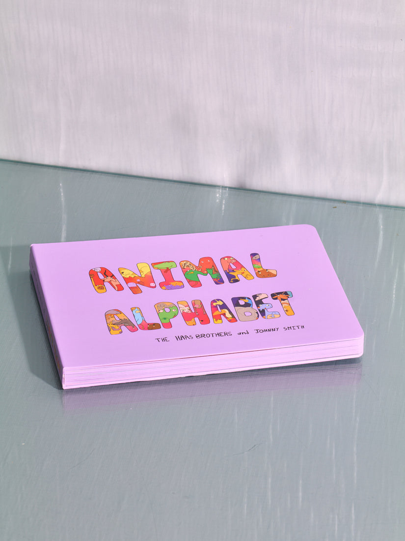 The Animal Alphabet book by the Haas Brothers and Johnny Smith lays across a glass surface. The lavender covers features bubble letters filled with illustrations of various animals.