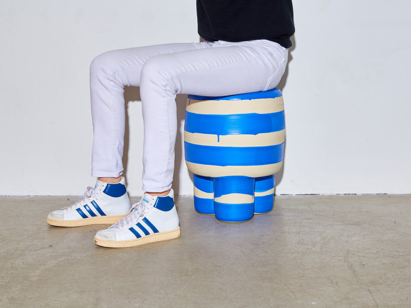 Someone sits on a blue Ceramic Milking Stool.