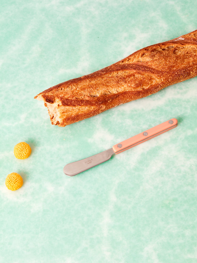 A torn baguette, two tangerine bonbons, and a pastel coral Sabre bistro spreader.