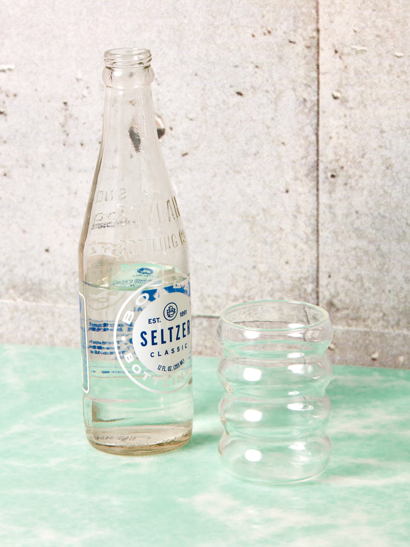 A bottle of seltzer sits next to a clear Ripple Glass.