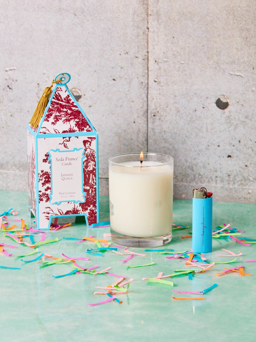 In a scatter of paper confetti sits a boxed Japanese Quince candle, the candle itself, and a blue Coming Soon lighter.