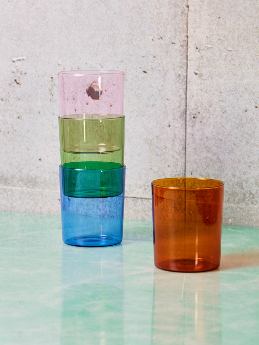 A stack of pink, green, and blue cups by Maison Balzac sitting next to a single amber cup.