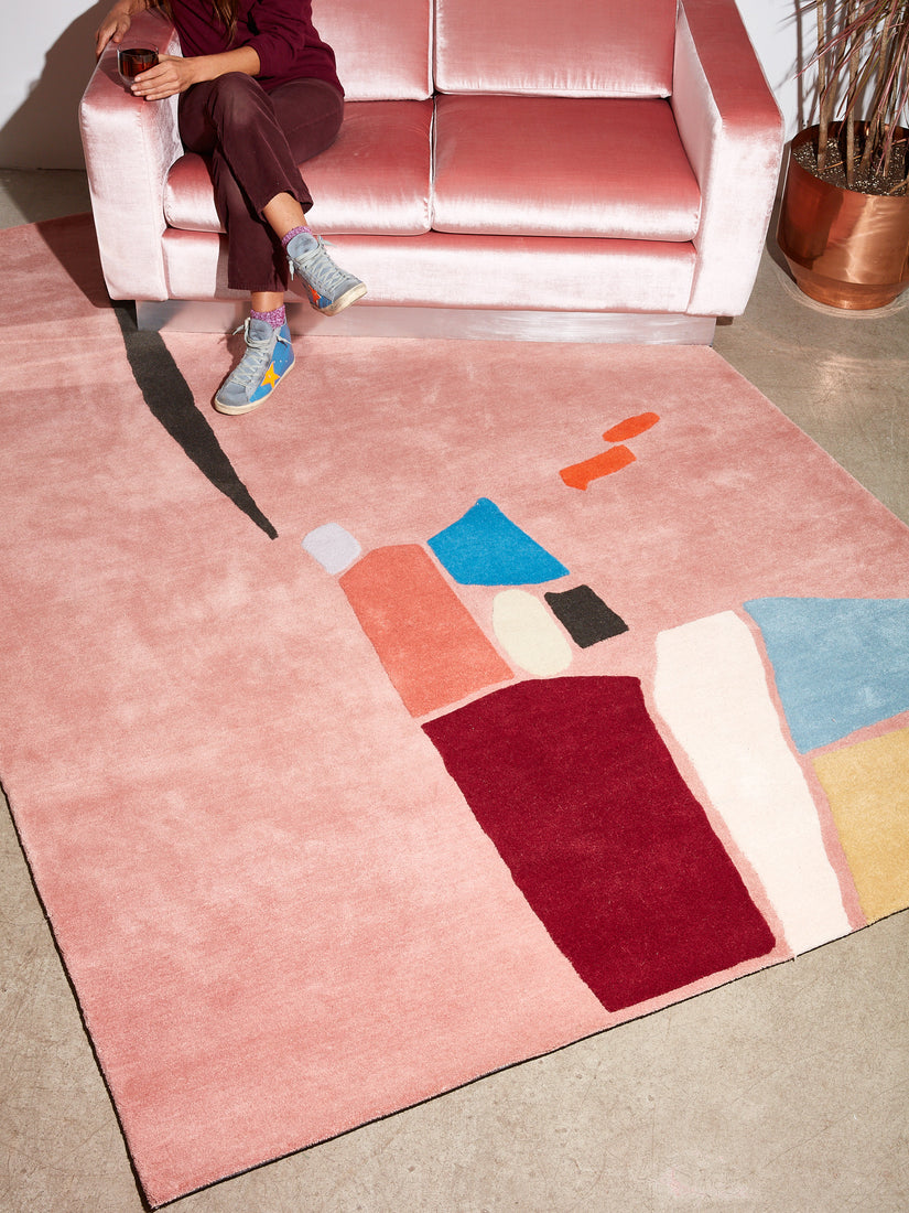 Salt Flats Rug sits diagonally under a pink velvet Milo Baughman Sofa. Someone sits atop the sofa with their legs crossed.