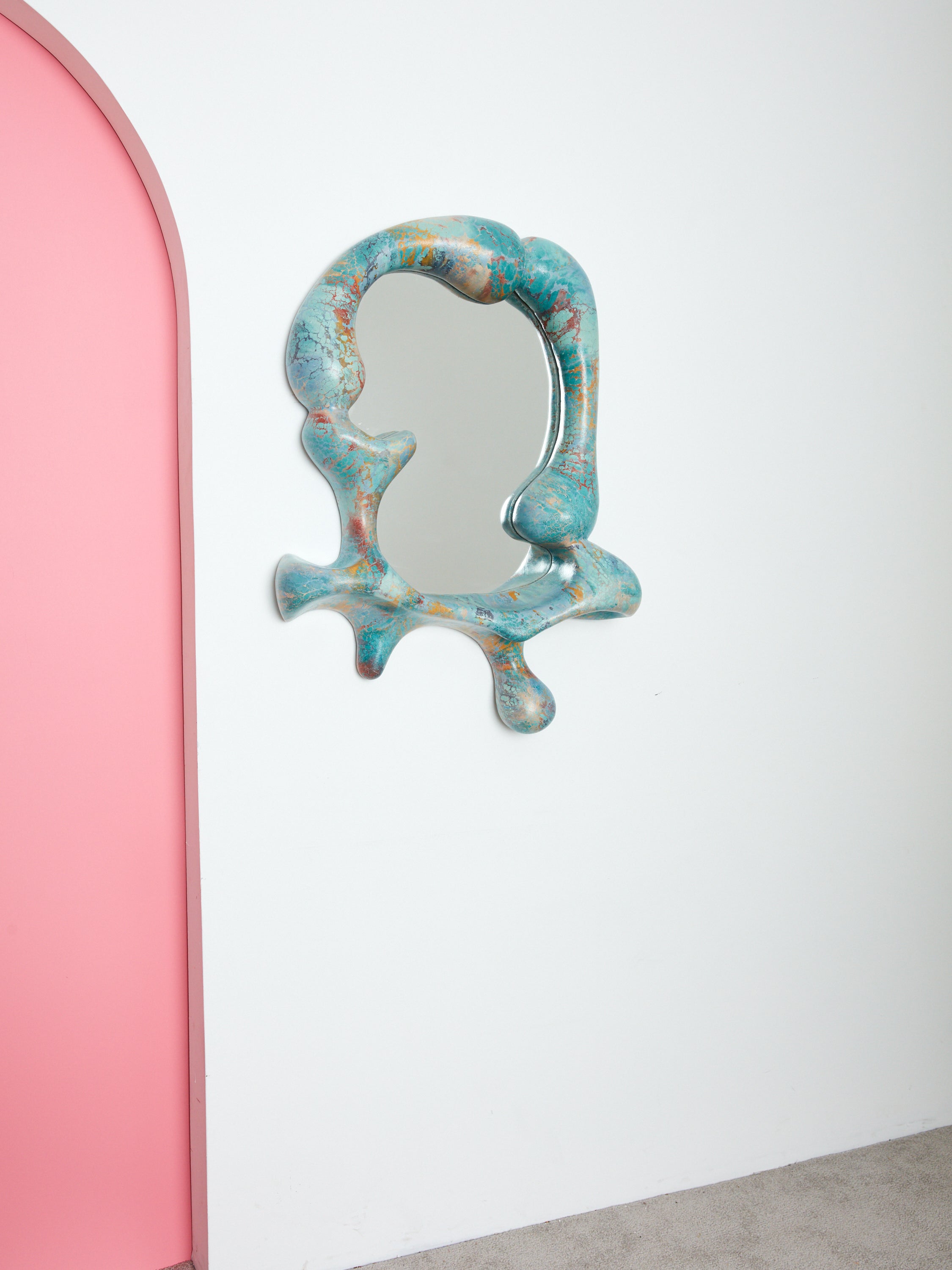 Blue Concrete Cat Iris mirror hung on a white wall beside a pink archway.