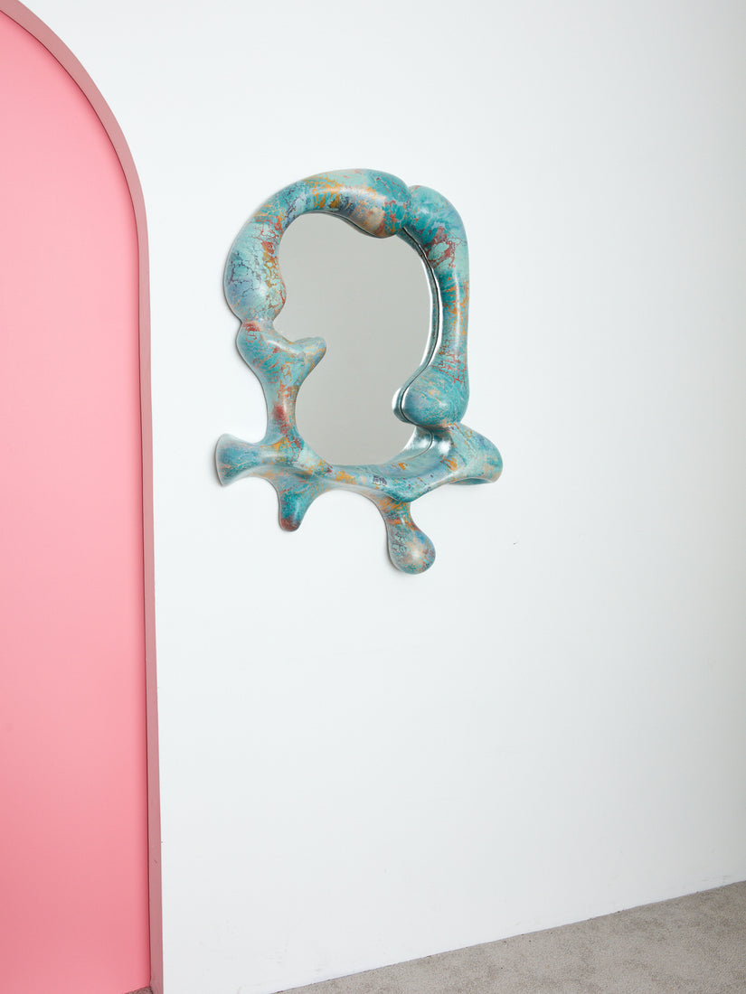 Blue Concrete Cat Iris mirror hung on a white wall beside a pink archway.