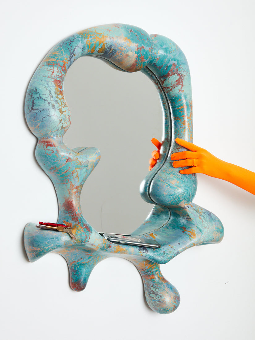 An orange gloved hand touches the frame of the Concrete Cat Iris Mirror.