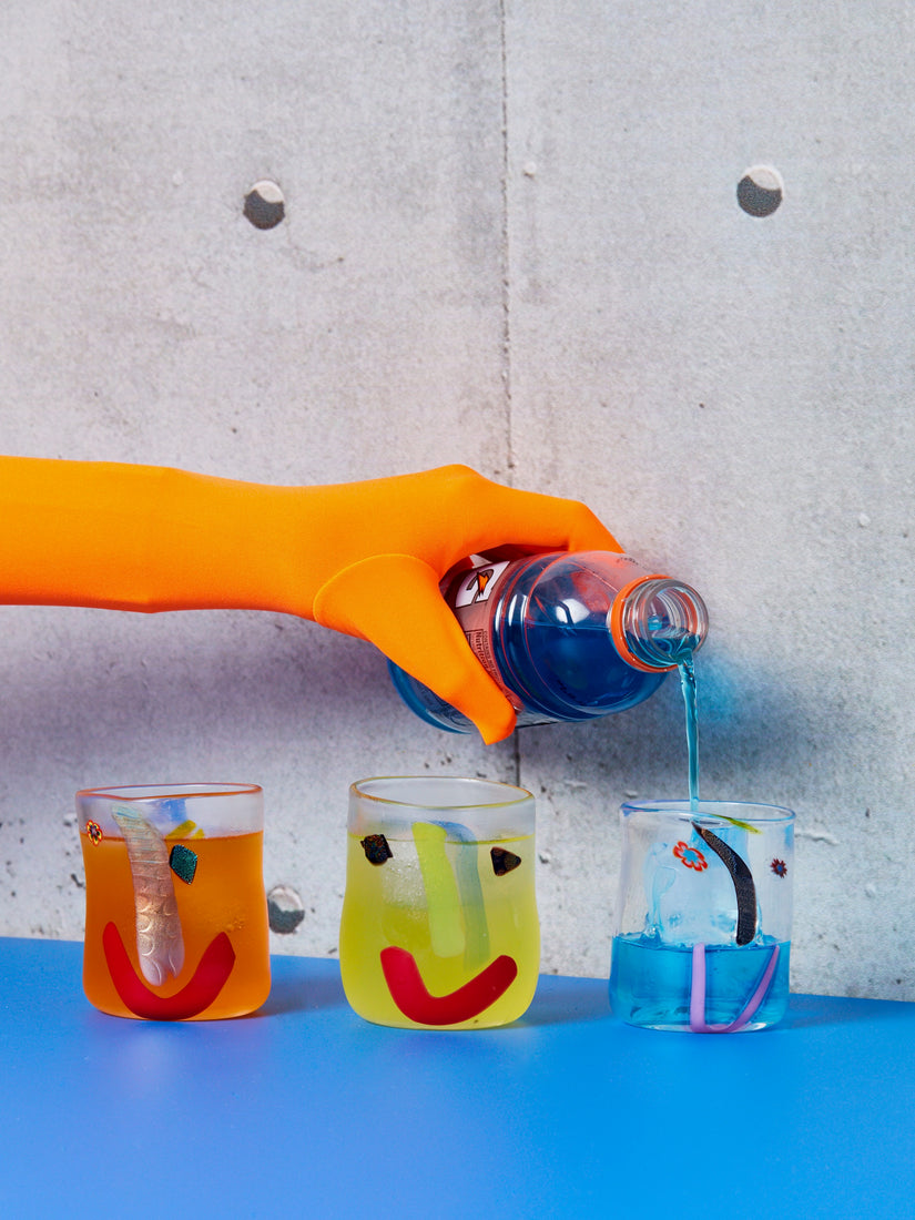 Three medium face vessel glasses, one full of an orange drink, one full of a yellow drink, and the right-most glass being poured of a blue gatorade by an orange gloved hand.