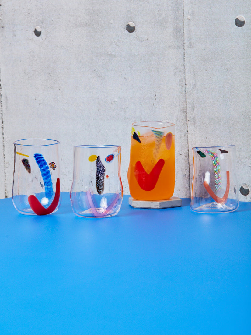 Four large face vessel glasses, one full of an orange drink sitting on top of a grey coaster.