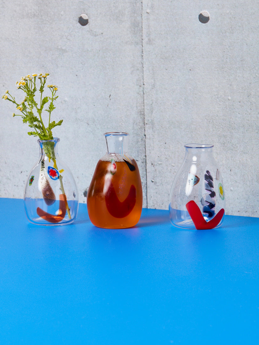 Three Face Carafe Vessels, one with flowers, one full of an amber liquid, and one empty.
