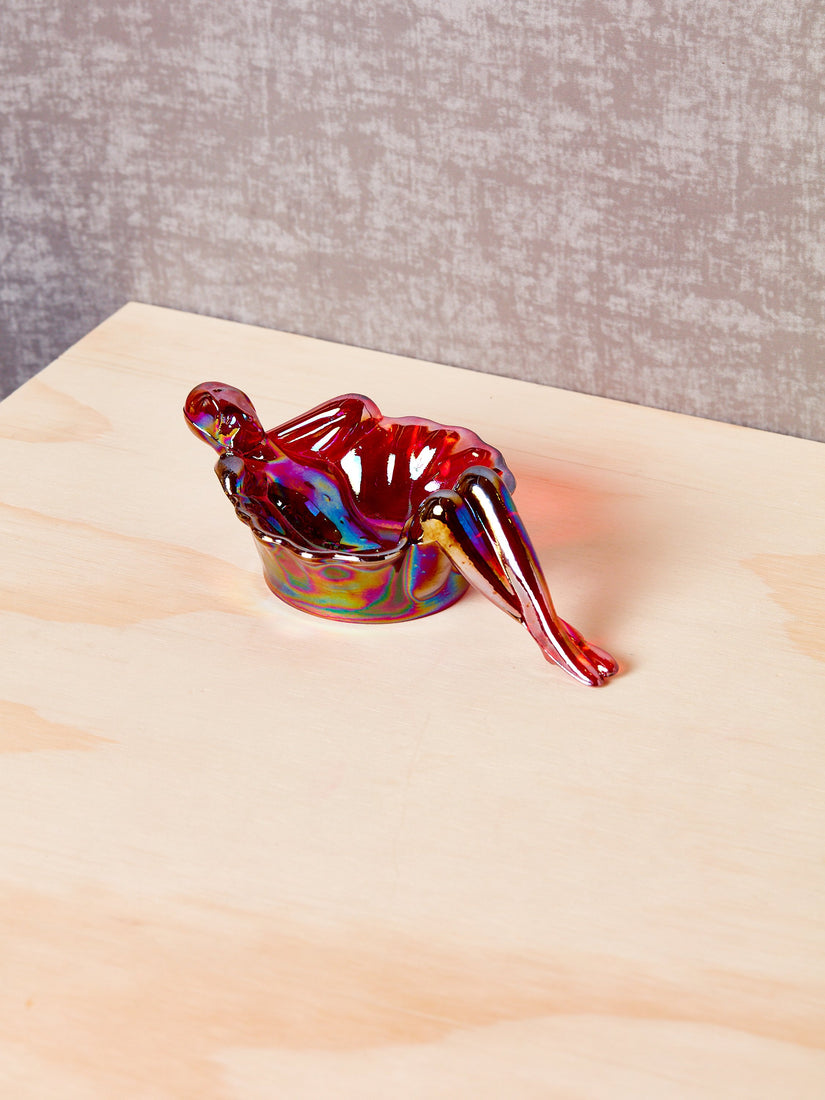A iridescent red bathing lady sitting on a pale wooden surface.