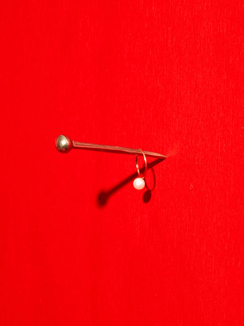 Hester the Nail hung on a vibrant red wall, with a pearl ring hanging on it.