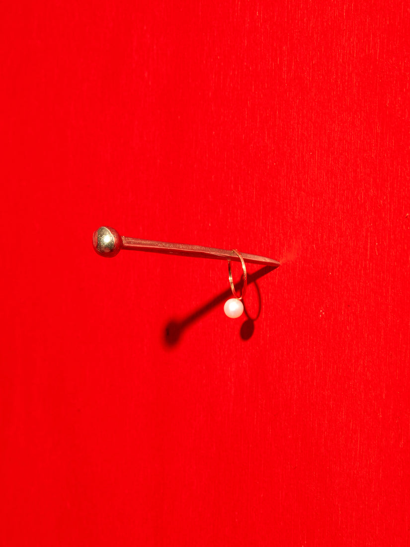 Hester the Nail hung on a vibrant red wall, with a pearl ring hanging on it.