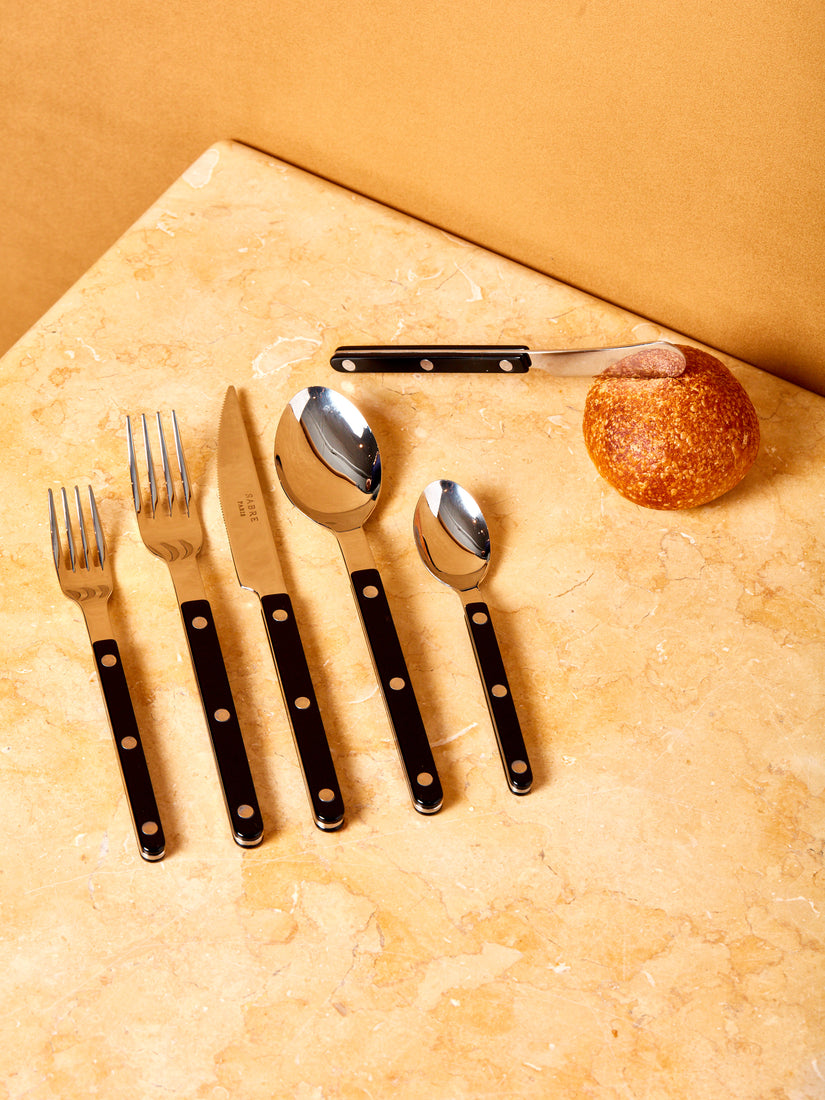 Six pieces of black bistro flatware by Sabre and a small boule of bread.