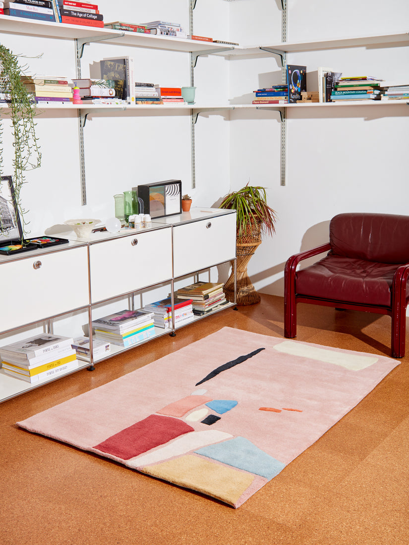 Salt Flats Rug by Cold Picnic styled in a living space amongst white shelves, storage, and a burgundy Gae Aulenti chair.