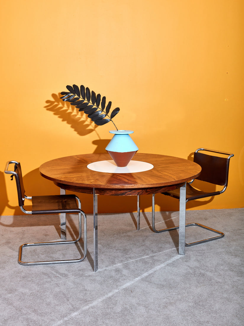 Two chrome cantilever chairs sit with the Rosewood Dining Table. In the center of the dining table is a BZippy vase with a black stem.