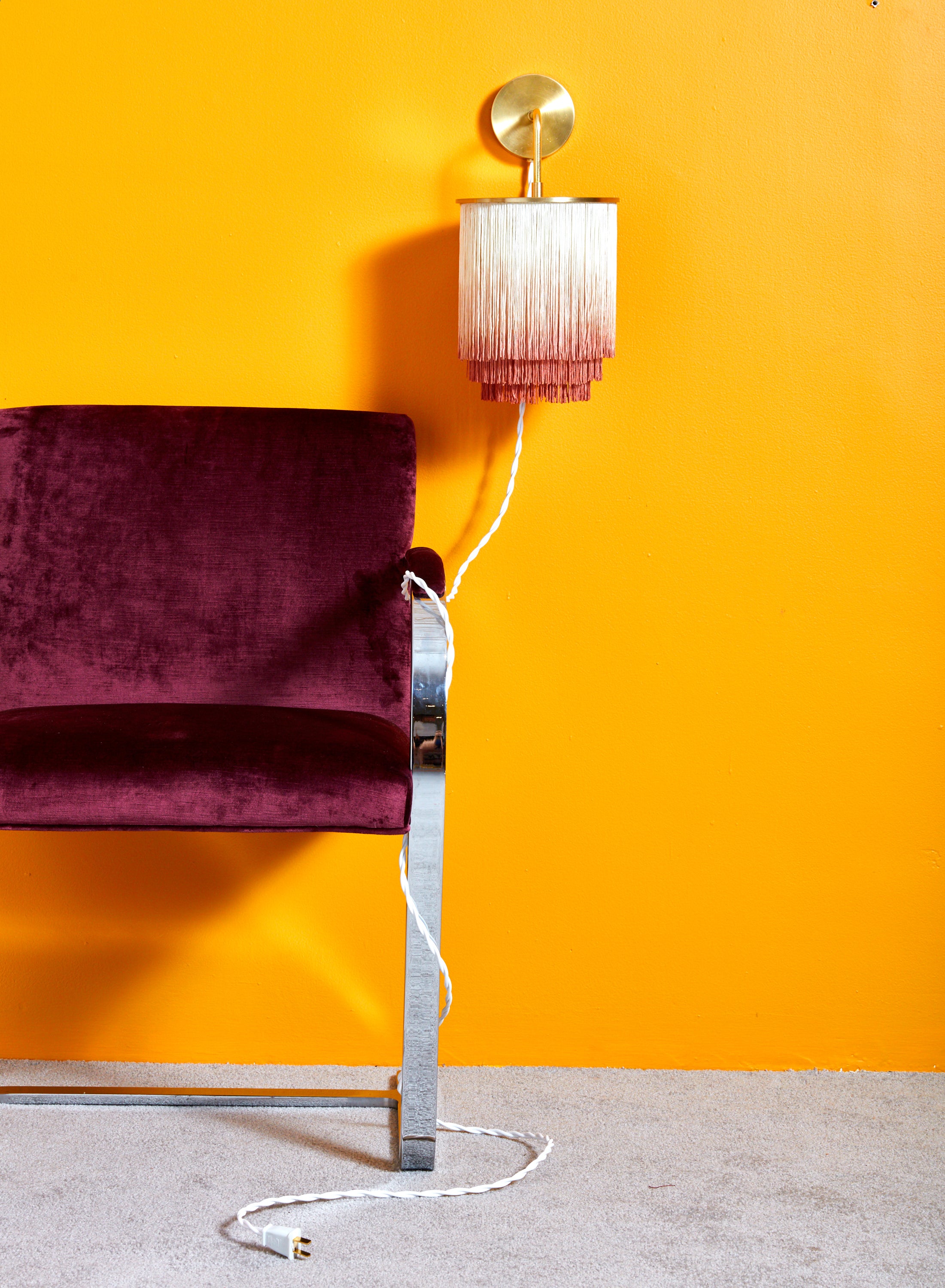 Fringe Wall Sconce mounted on a marigold wall with its cord wrapped around the leg of a flatbar BRNO chair.