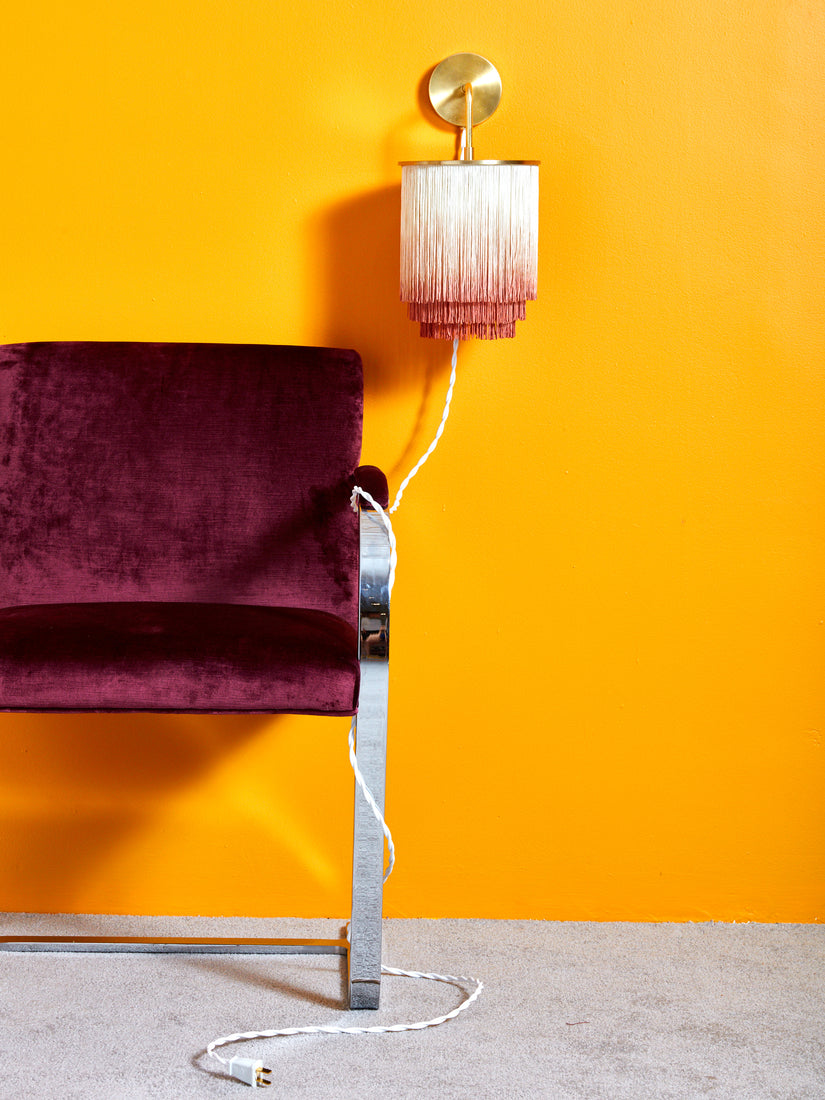 Fringe Wall Sconce mounted on a marigold wall with its cord wrapped around the leg of a flatbar BRNO chair.