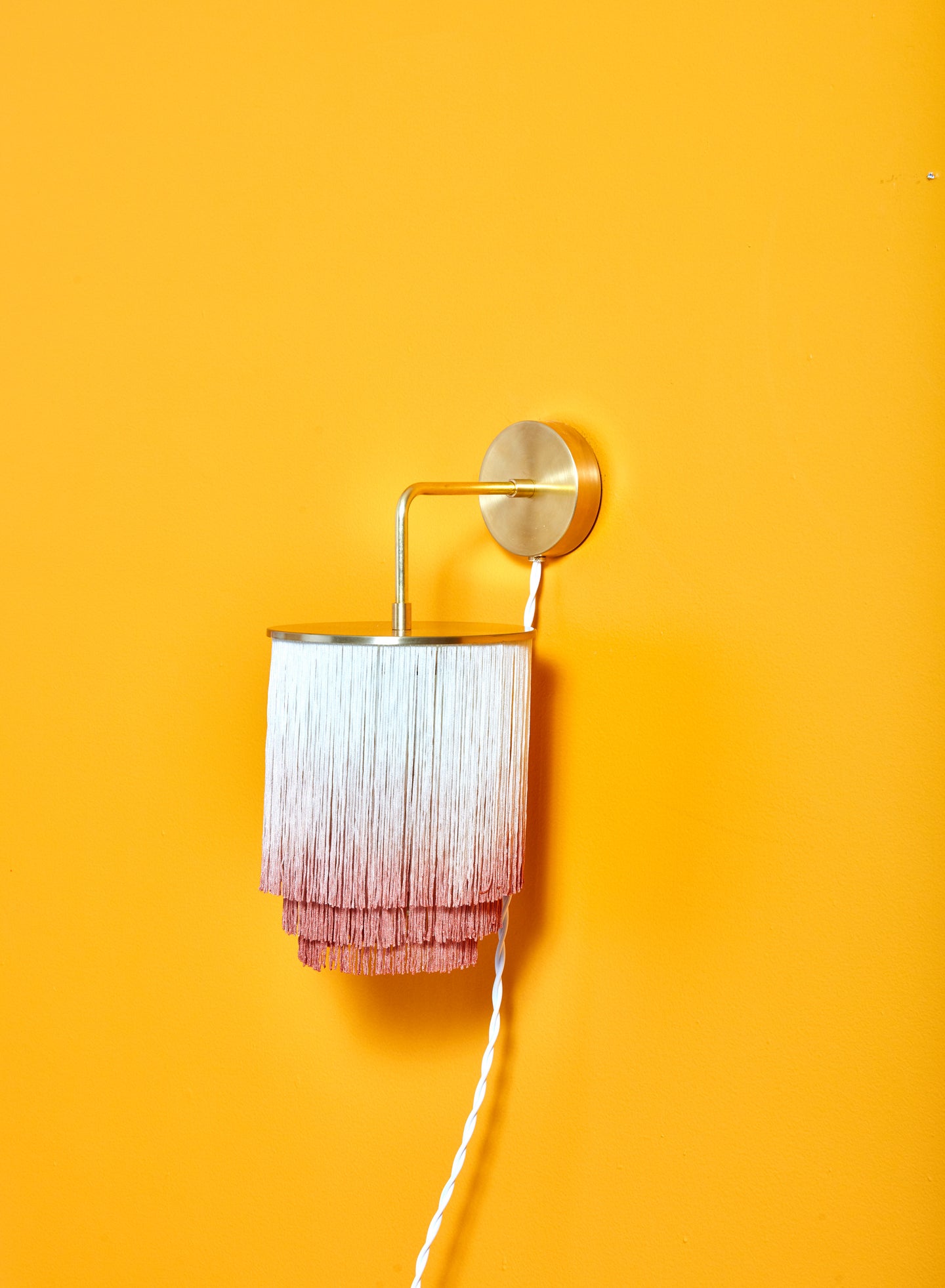 Brass wall sconce with cream to pink fringe shade.