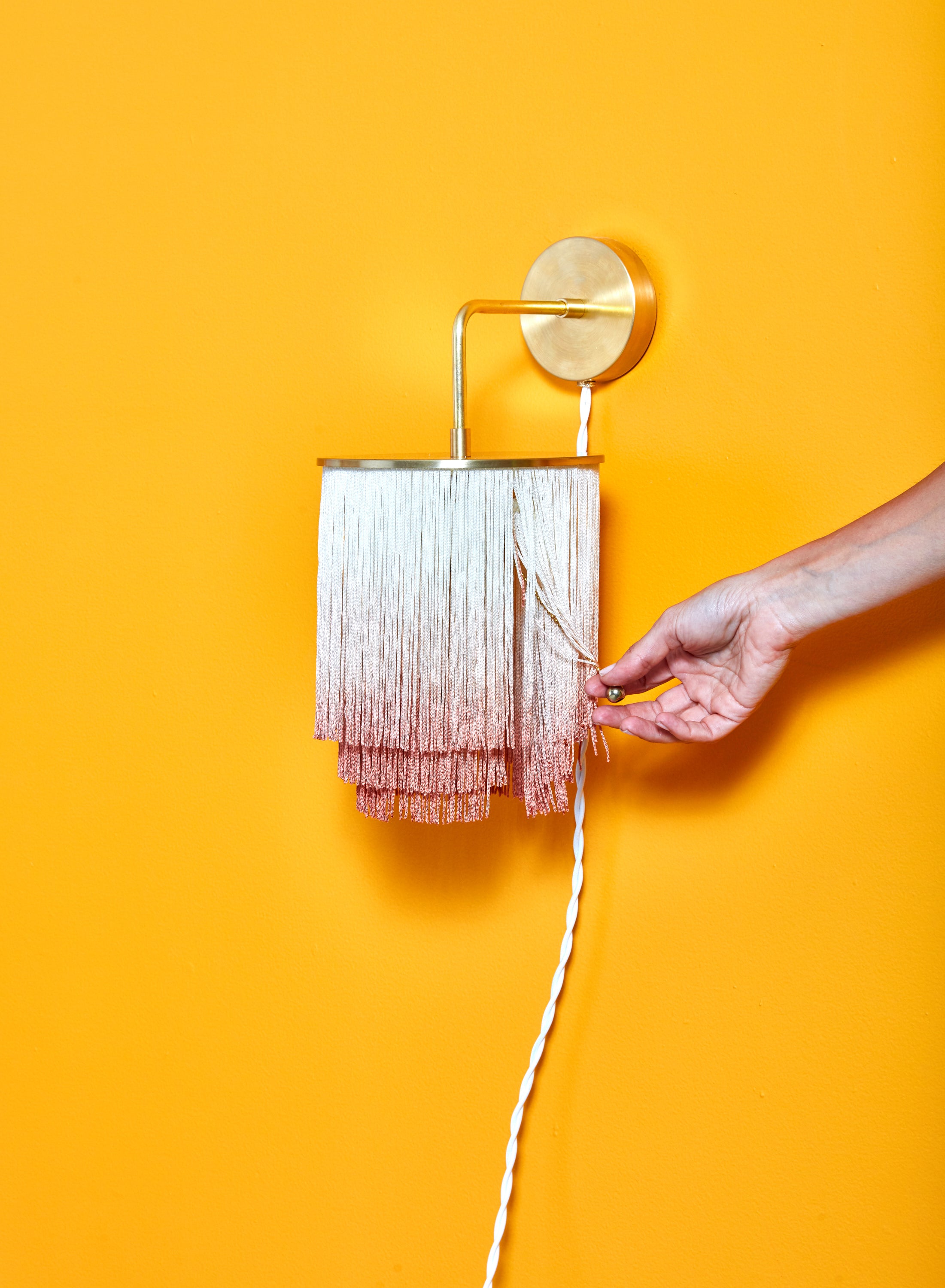 A hand pulls at the hidden ball chain switch of the Fringe Wall Sconce by Huldra of Norway.