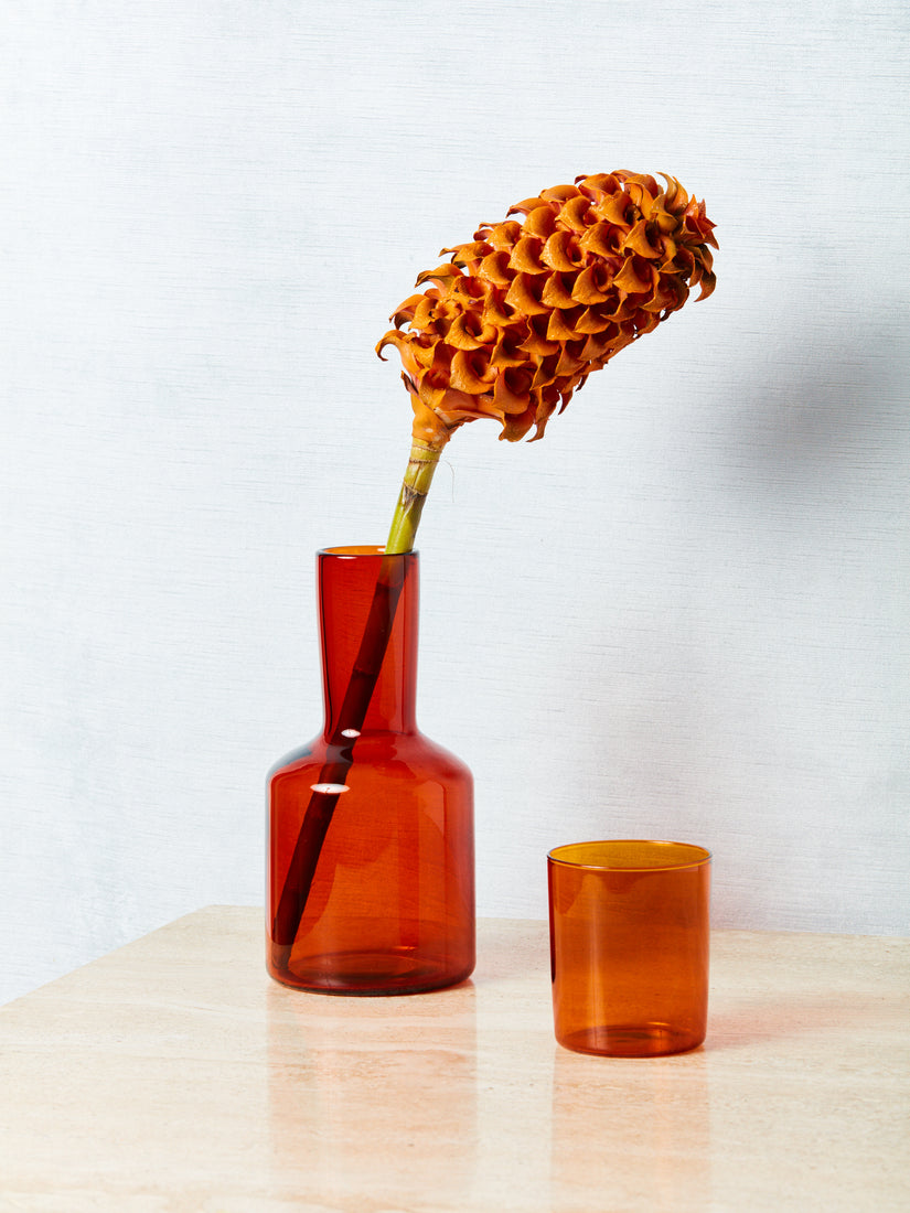 An amber bedside carafe with its cup off and a flower inside the carafe.