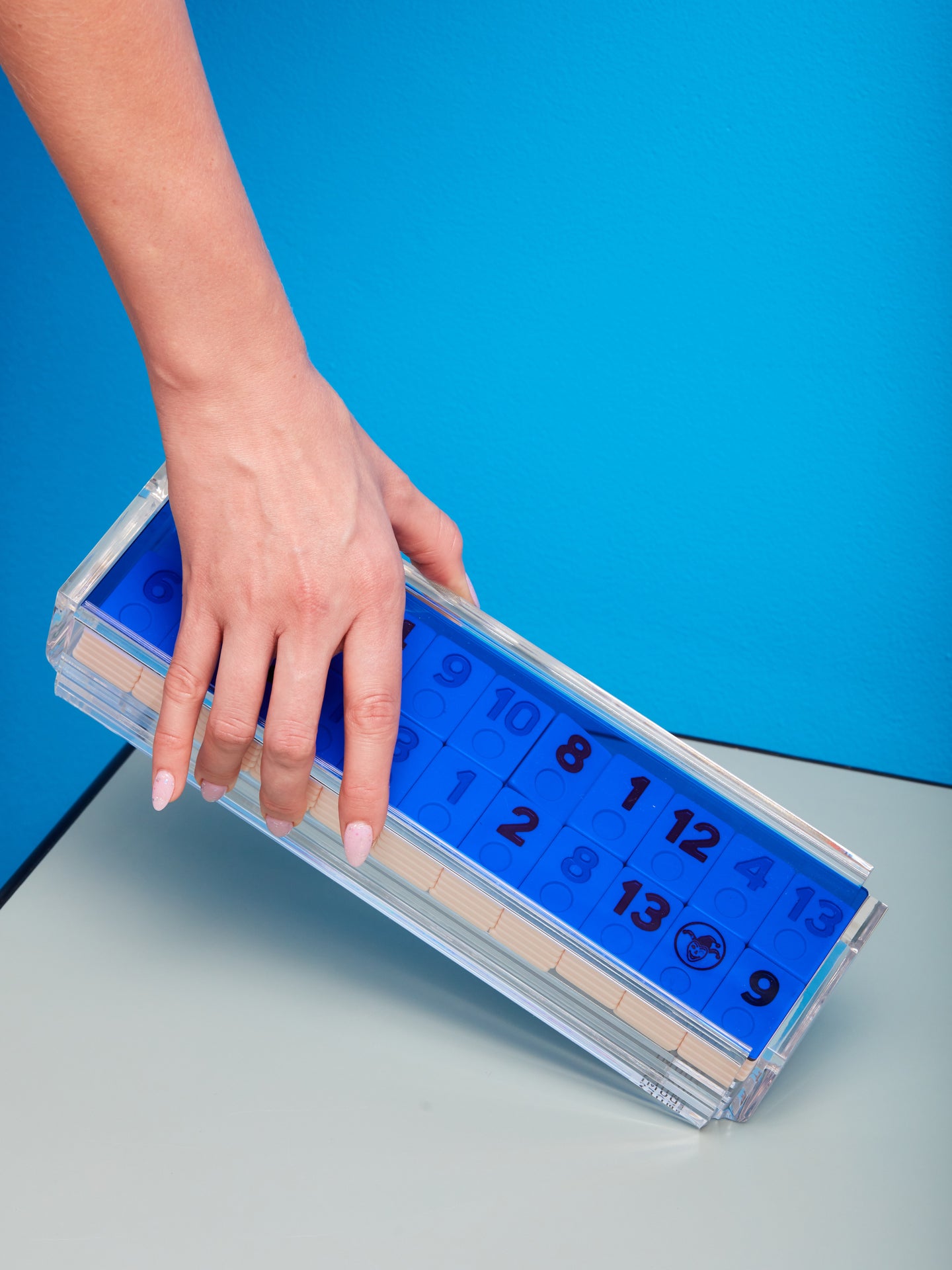 A hand gently hold up a Blue Rummy Tile Game by Luxe Dominoes.