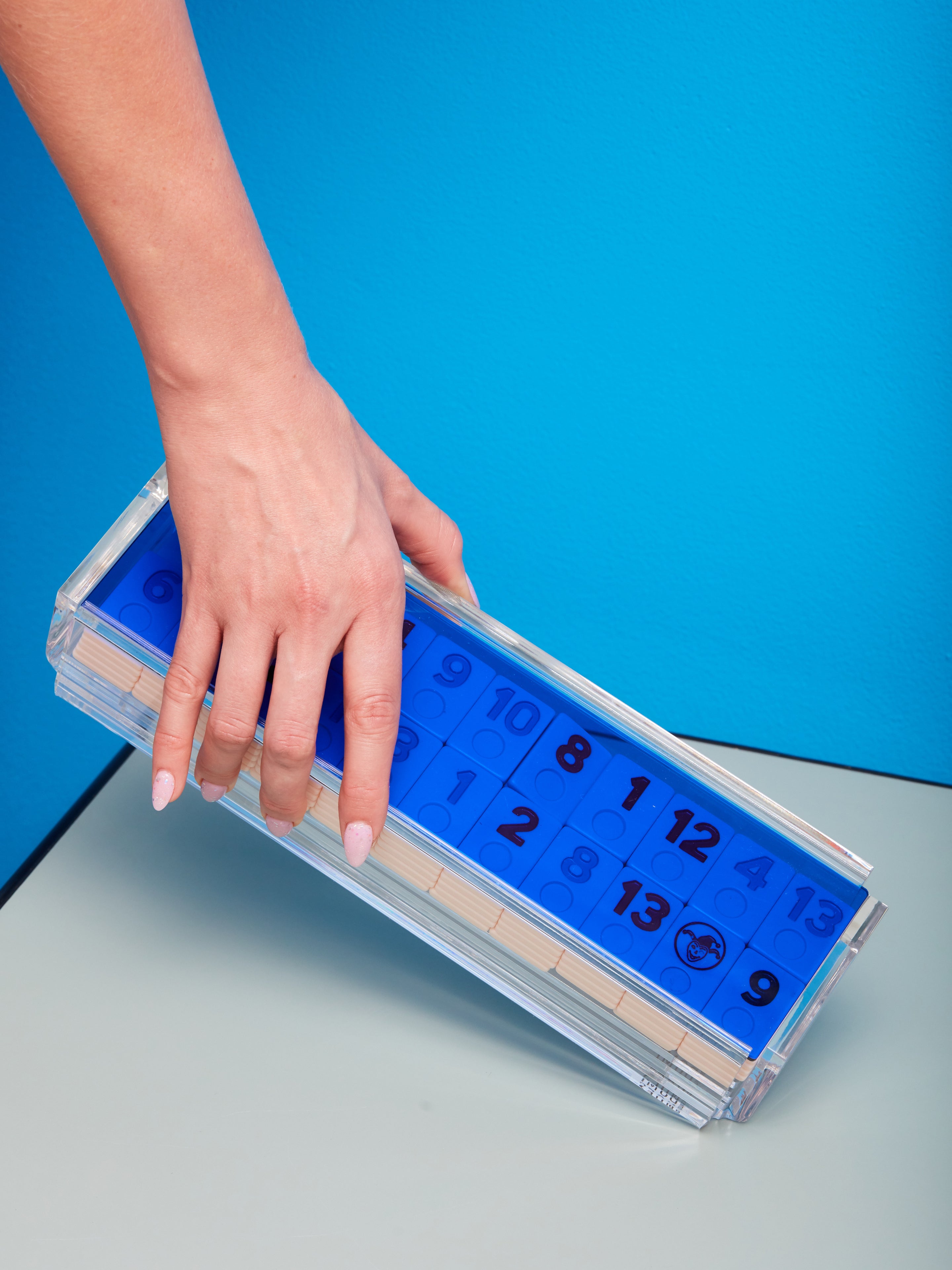 A hand gently hold up a Blue Rummy Tile Game by Luxe Dominoes.