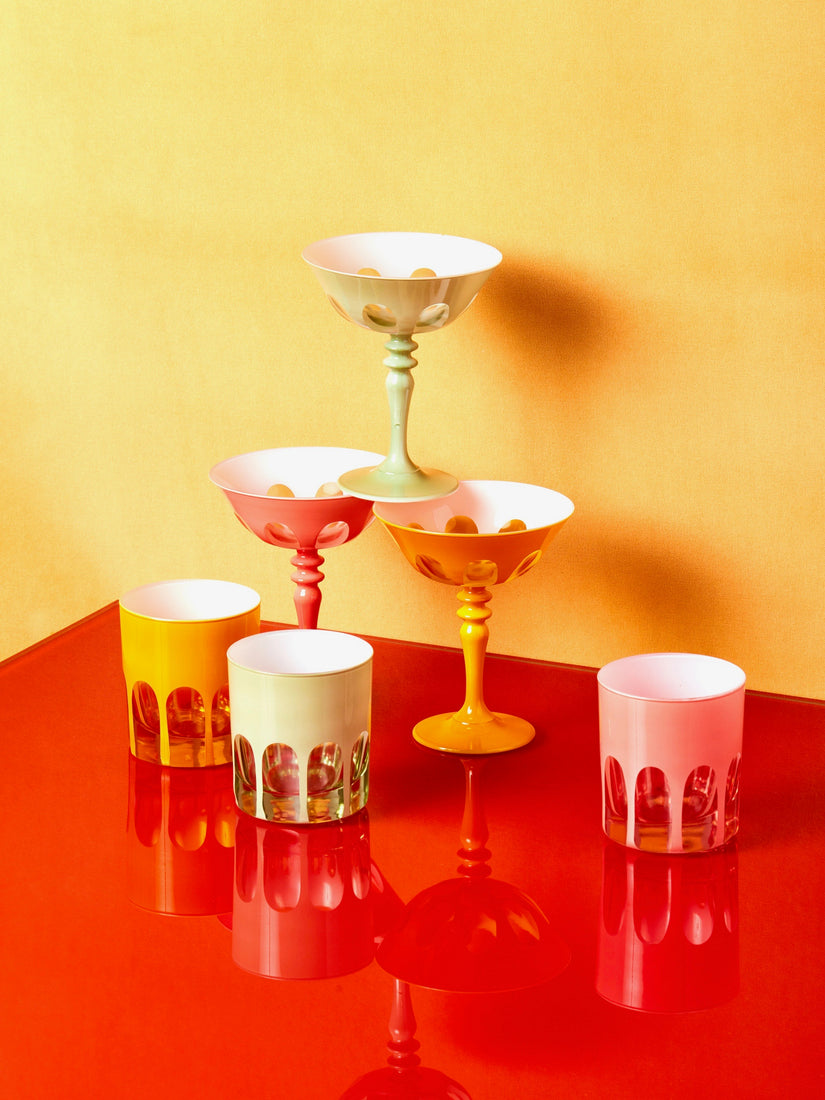 Rialto Old Fashioned and Coupe Glasses by Sir Madam stacked and displayed on a red glossy surface.