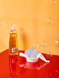 A white bathing lady dish with a silver sponge inside of it. Bubbles and soap surround the dish.