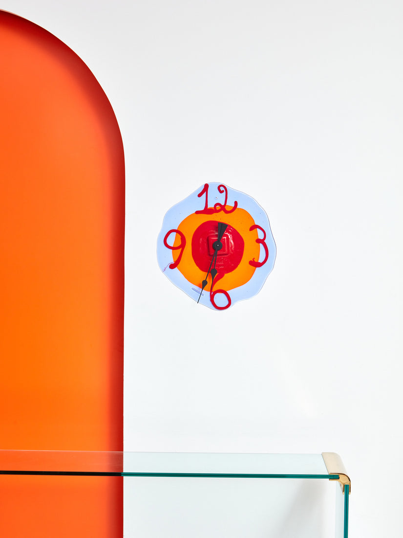 Watch Me Clock hung on a wall beside an orange archway above a glass console table.