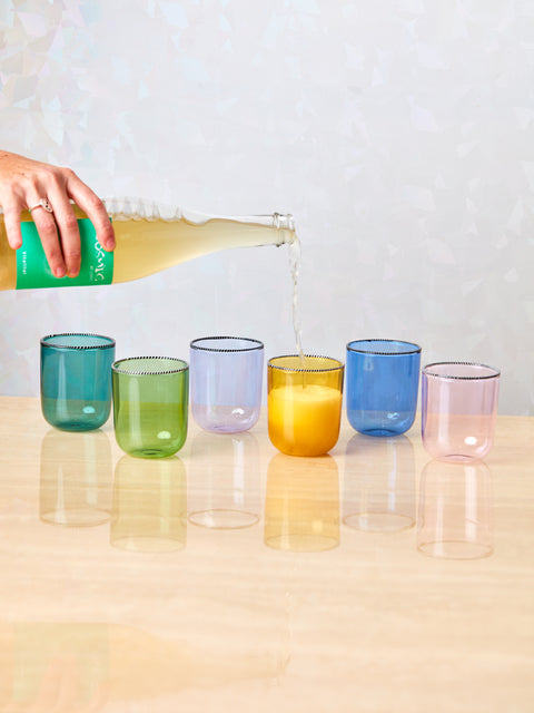 A hand pours a bottle of white wine into a set of Striped Rim Glasses by Fredericks and Mae.