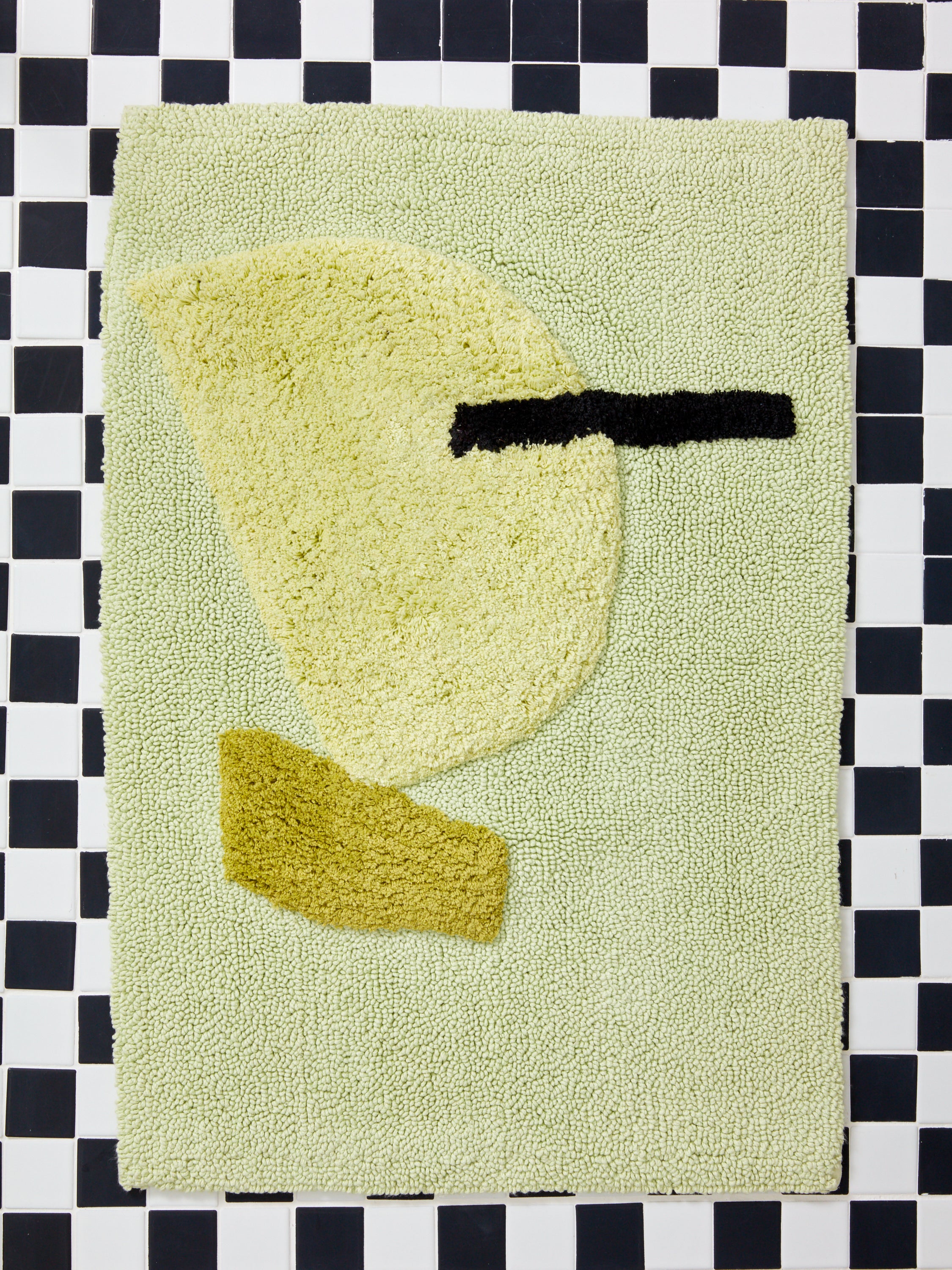 Medium Cool Bath Mat by Cold Picnic against a black and white tiled surface.
