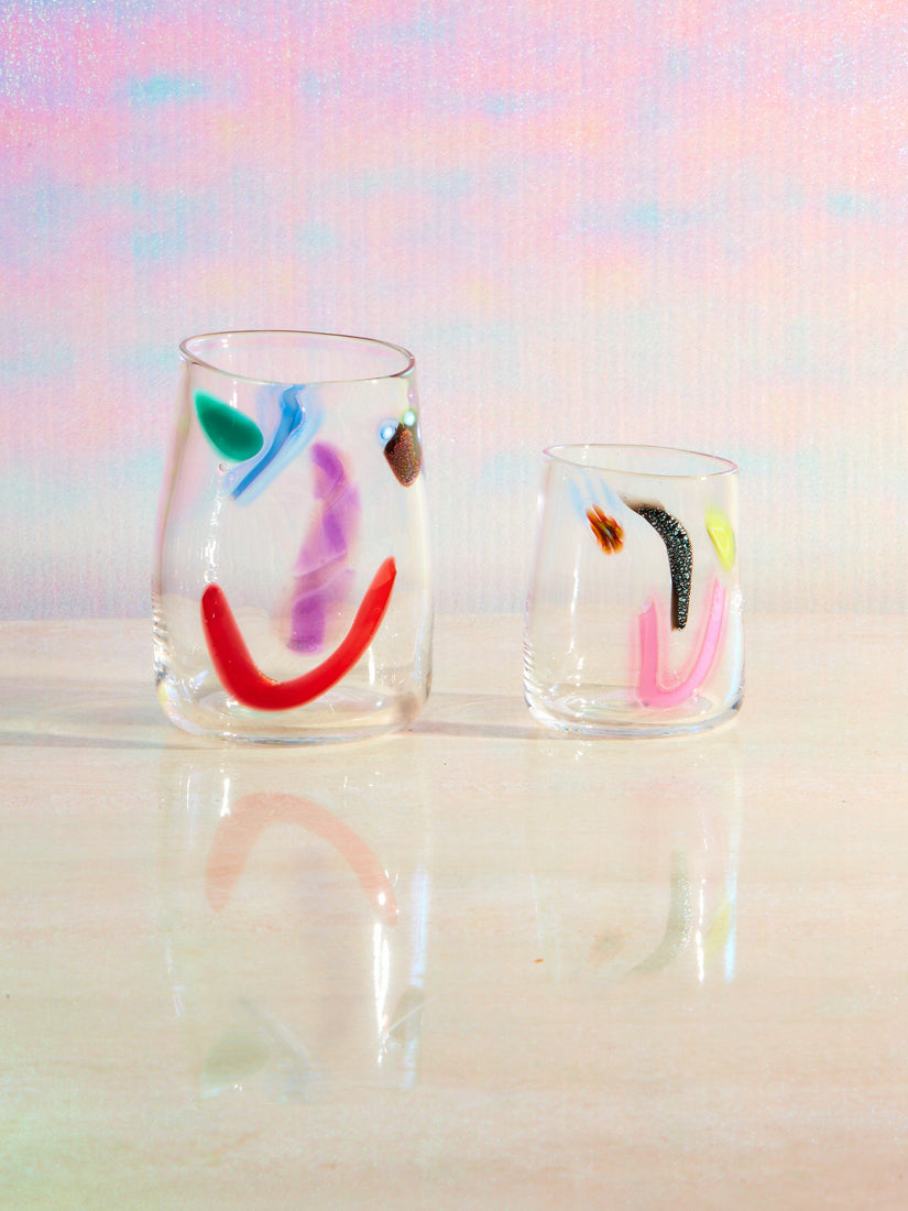 Two hand blown glass face vessels by degen with different multicolored glass smiley faces.