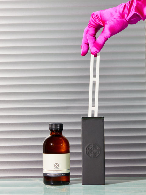 A pink satin gloved hand pinches the porcelain reed of the Kitowa diffuser.