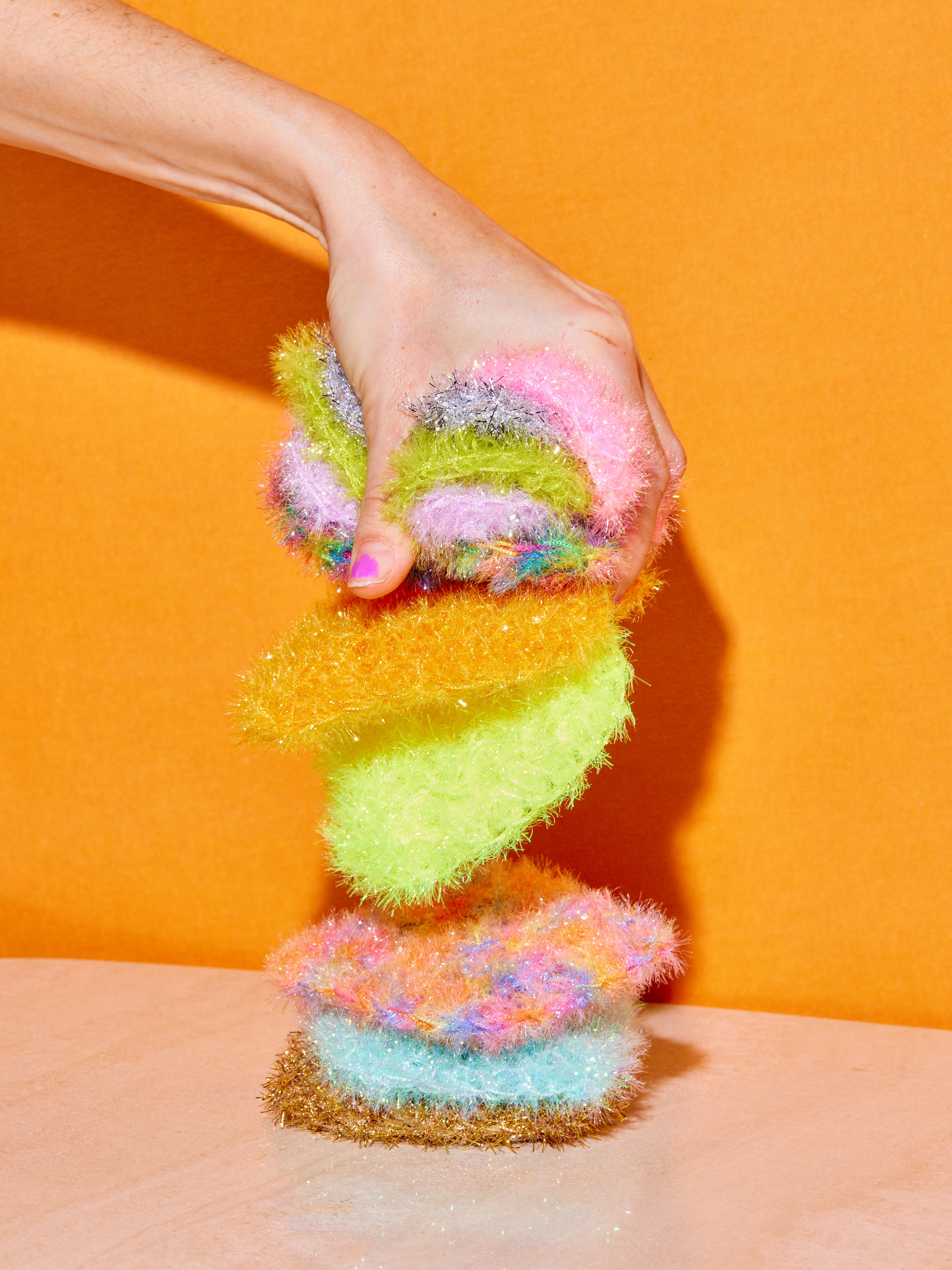 A hand grabbing a stack of ten different colored crocheted sponges.